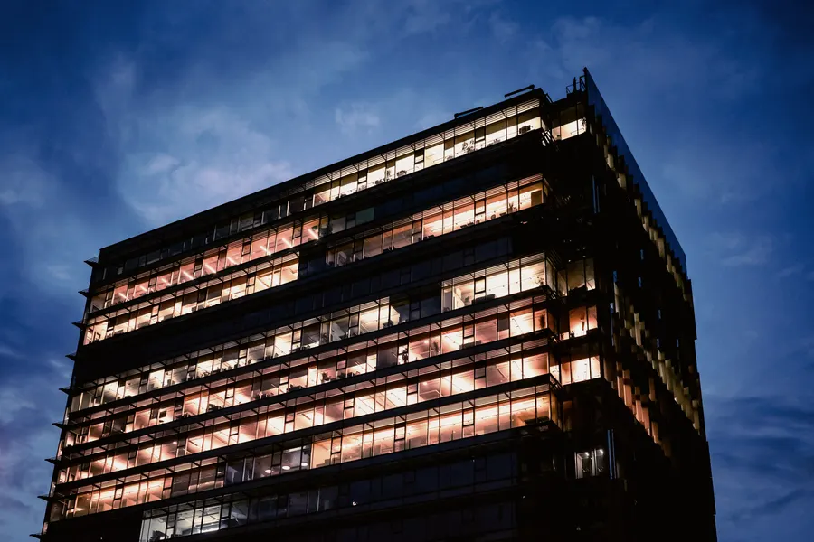 A modern office building with glowing windows against a deep blue evening sky