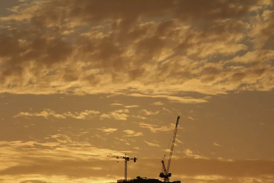 Construction cranes silhouetted against an orange sunset